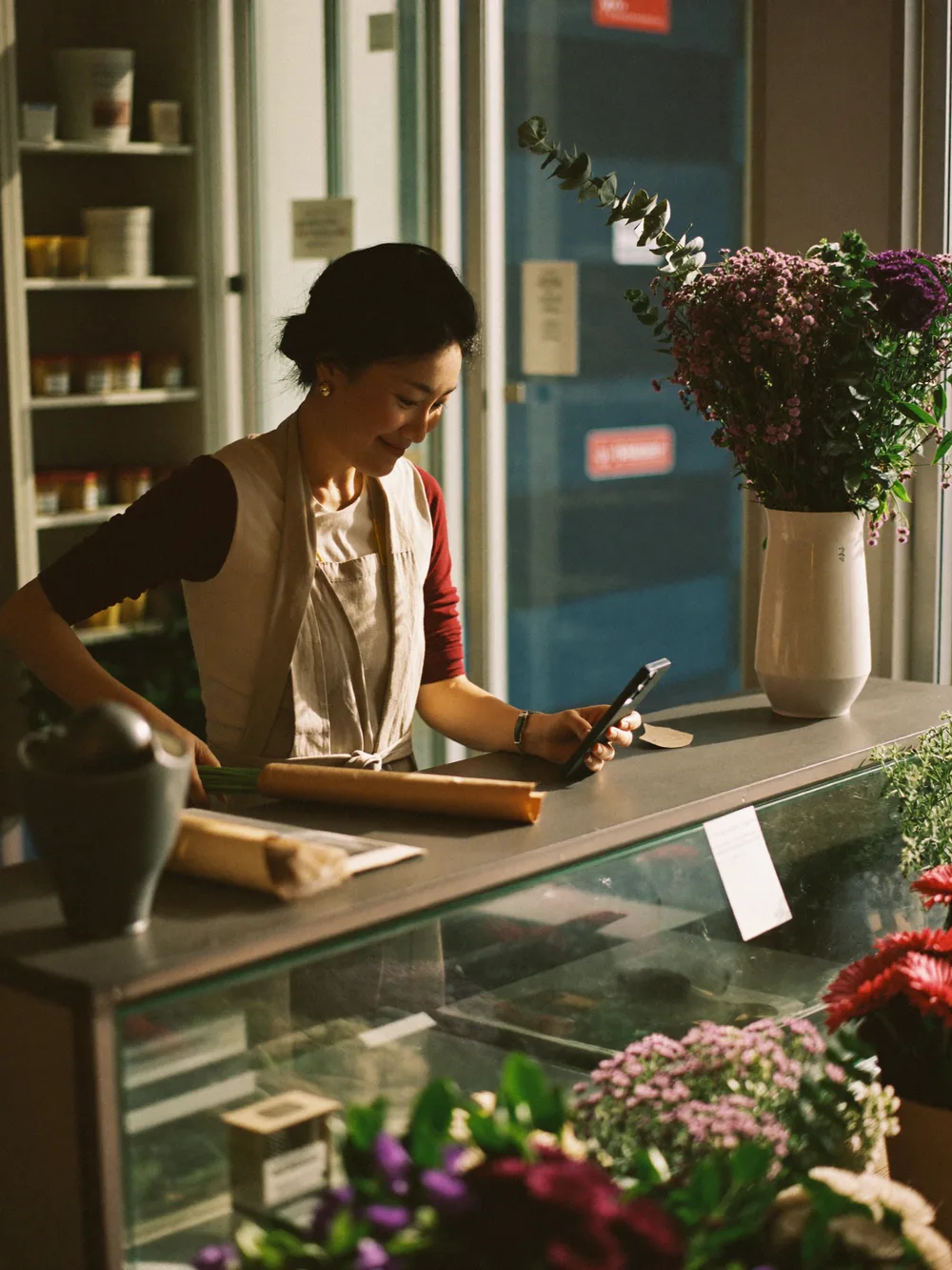 A florist wraps a bouquet at her counter while ReplyArc answers a customer on her phone